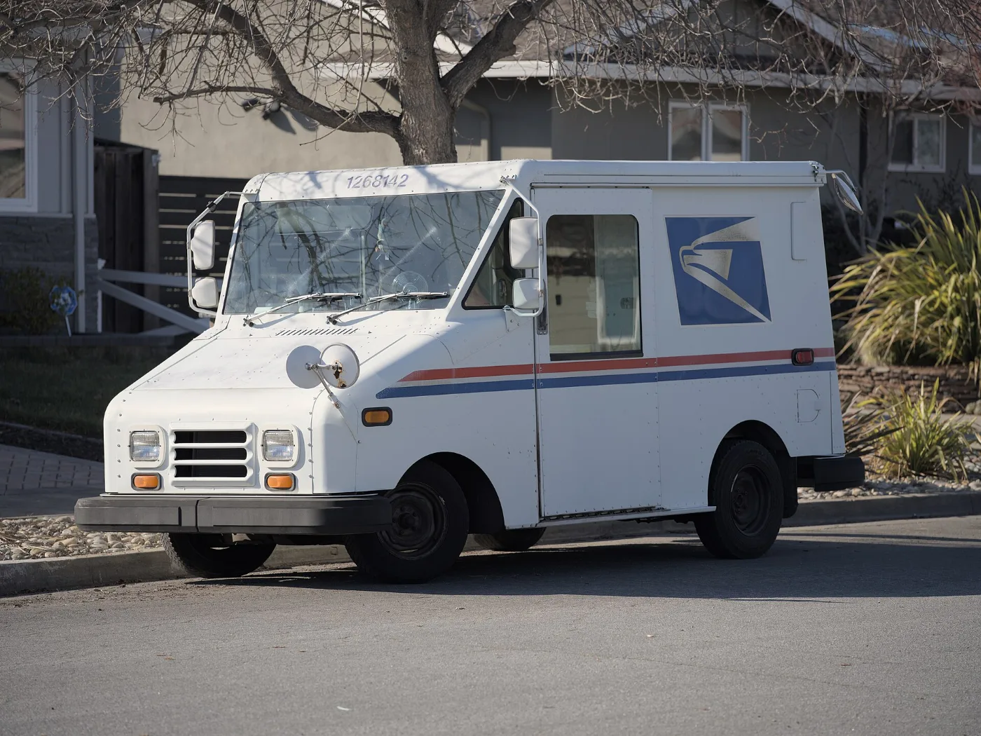 Camión del servicio postal en una calle residencial, como el que trae el título del carro por correo